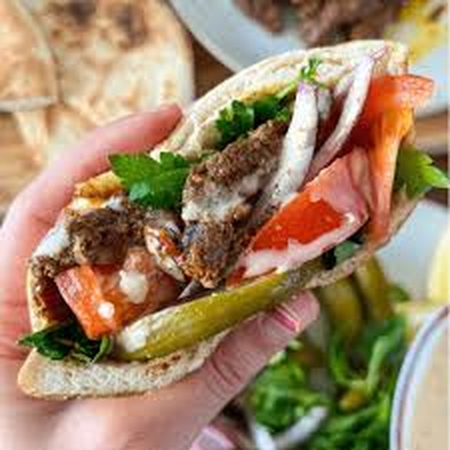 A hand holding a filled pita sandwich