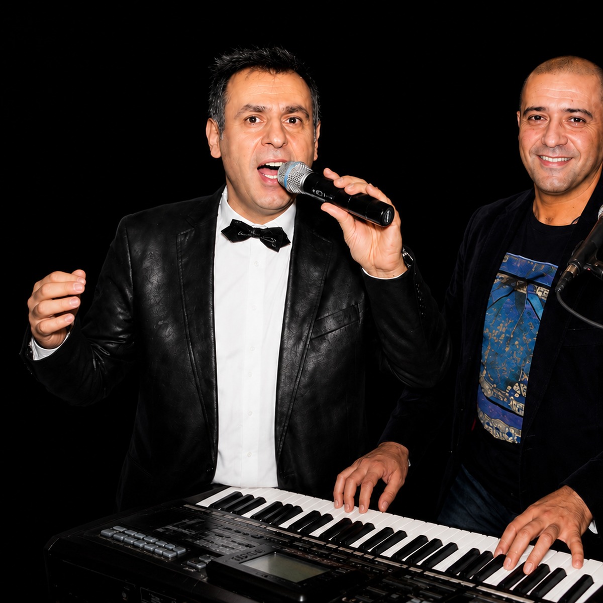 Two musicians performing, one singing into a microphone at a keyboard